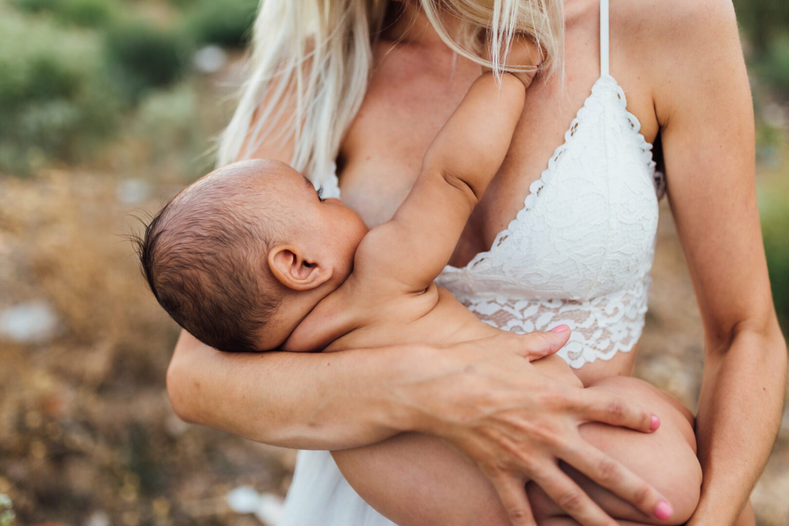 Young blond woman breastfeeding her mixed race baby. They are in the field one summer afternoon. She wears a white top and the baby is naked.