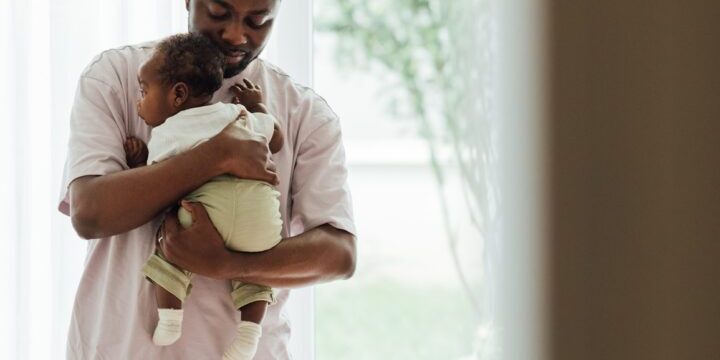 Attractive young man, father holding his infant in his arms at home in bedroom