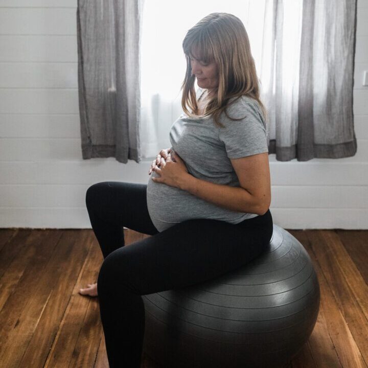 full term (39 week) pregnant woman sitting and bouncing on an exercise as is currently recommended to assist baby move into position for labour. woman is in lounge wear