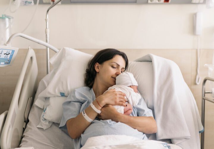 Woman lying on a hospital bed in a neonatal department holding her newborn baby as they both sleep. Maternity concept.